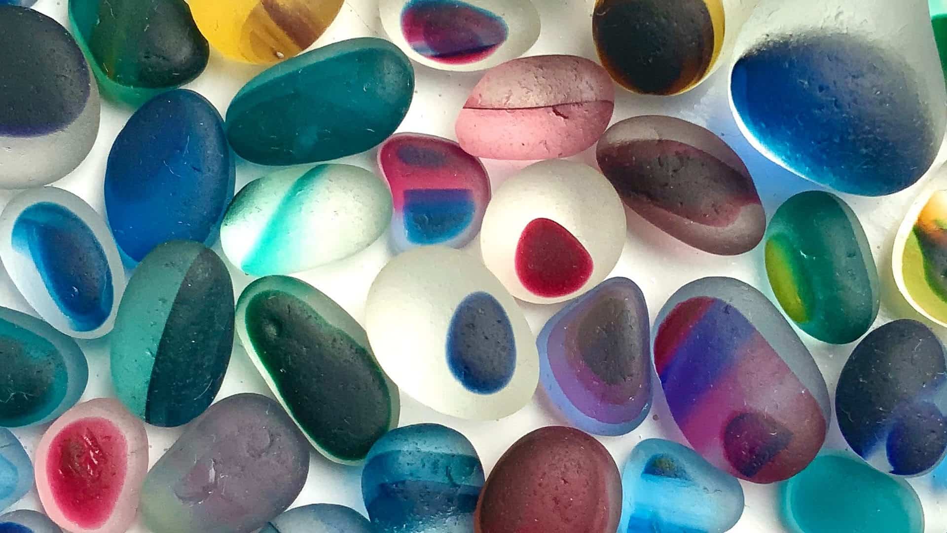 Seaglass pieces in various colours and shapes scattered on a white surface.