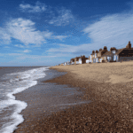 Aldeburgh seaglass beach with pebble shoreline and coastal houses under blue sky.