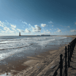 Seaside promenade along the coast with a lighthouse in the distance, perfect for sea glass hunting a.
