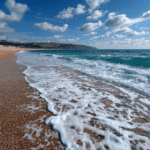 Seaglass on sandy beach with waves and cliffs in background.